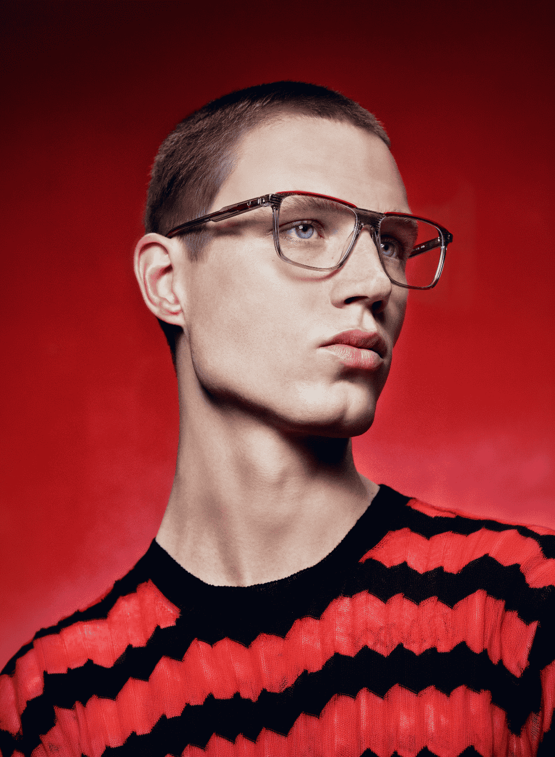 Portrait of a person wearing glasses and a black-and-red striped sweater against a red background