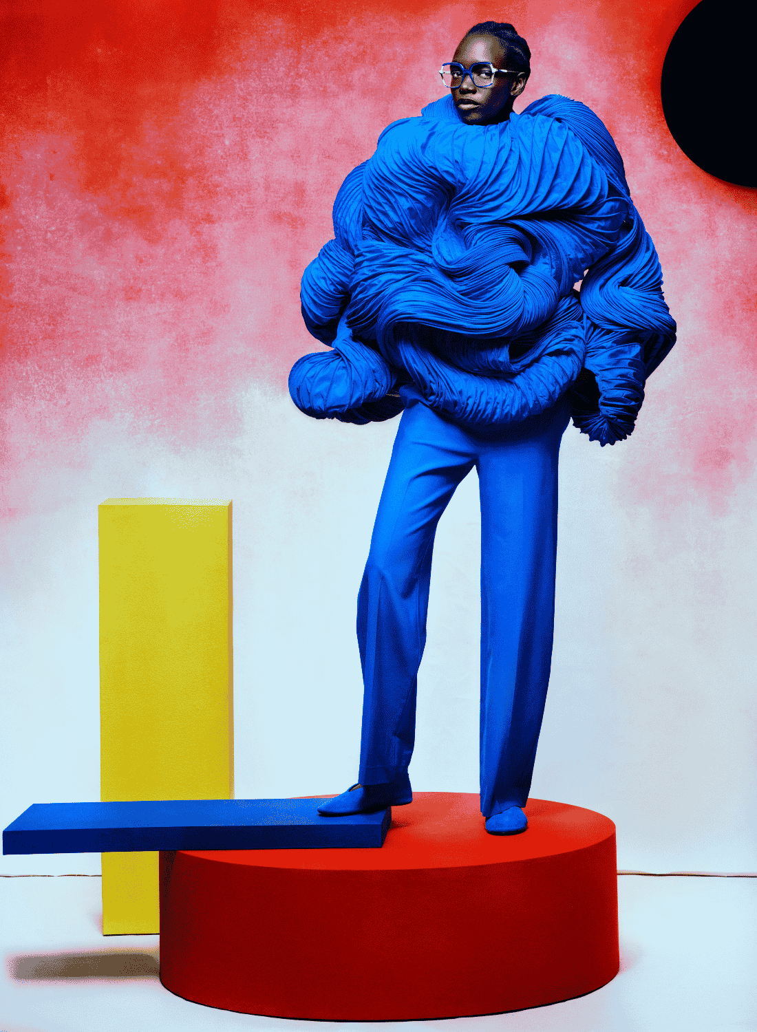 Person in bright blue outfit standing on a red platform against a red-and-white background