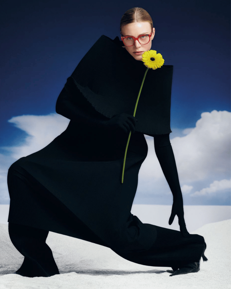 A woman wearing glasses, in a black dress is holding a yellow flower