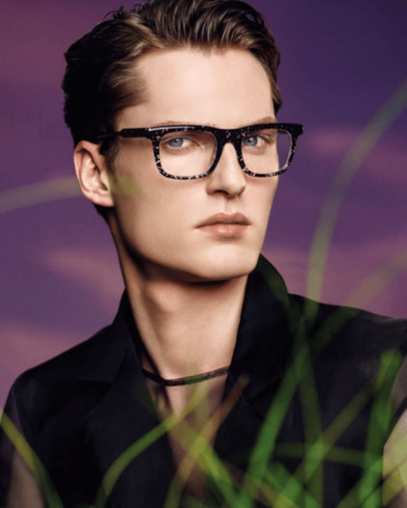 A man wearing glasses and a black jacket is standing in the grass.
