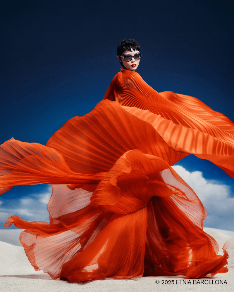 A woman wearing sunglasses in an orange dress with a blue sky in the background