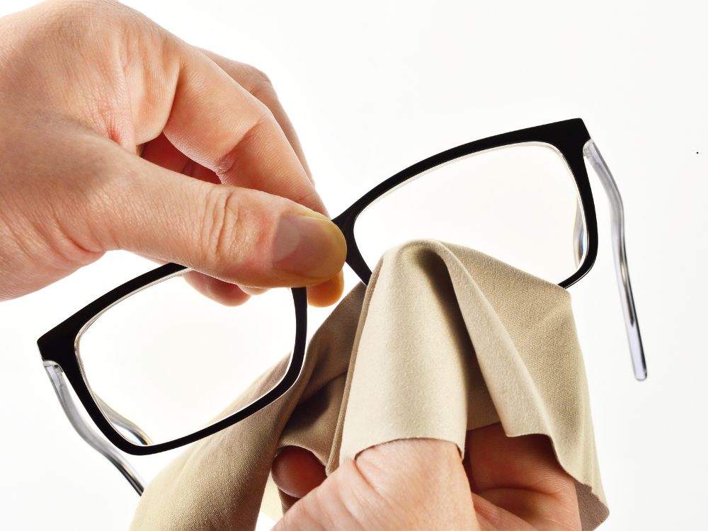 A person is cleaning a pair of glasses with a cloth