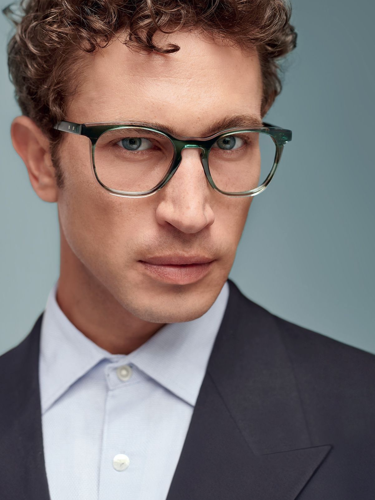 A man wearing glasses and a suit is looking at the camera
