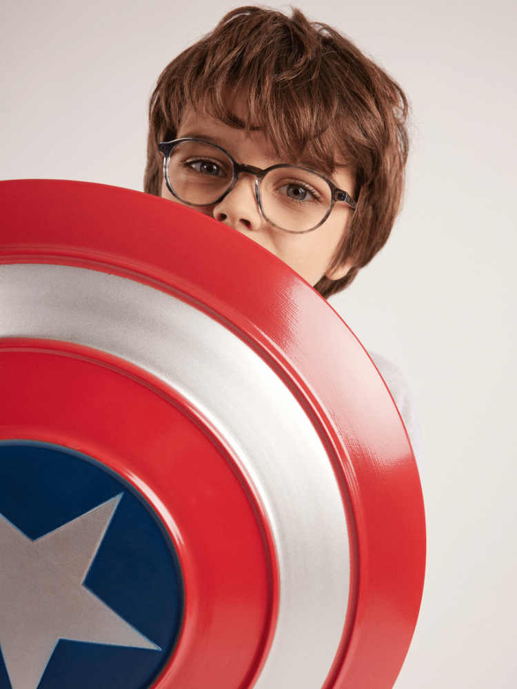 A young boy wearing glasses is holding a captain american shield