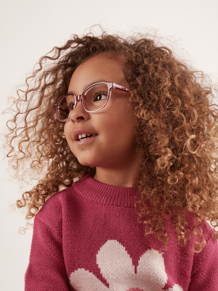 A little girl wearing glasses and a pink sweater with a flower on it.