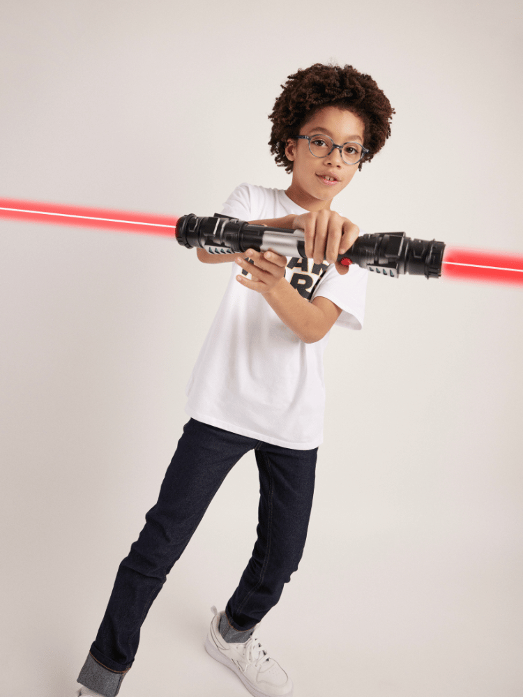 A young boy wearing glasses is holding a red light saber in his hands.