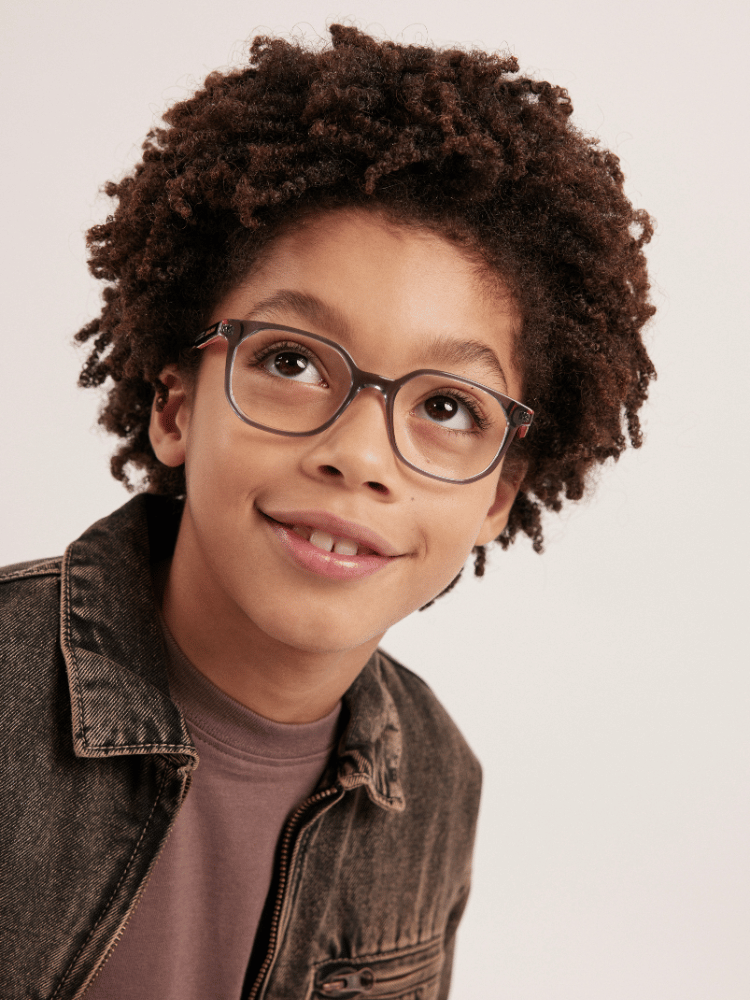 A young boy wearing glasses and a denim jacket is smiling.