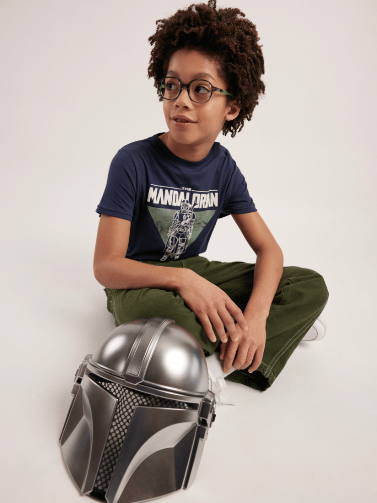 A young boy is wearing glasses and sitting on the floor next to a helmet.