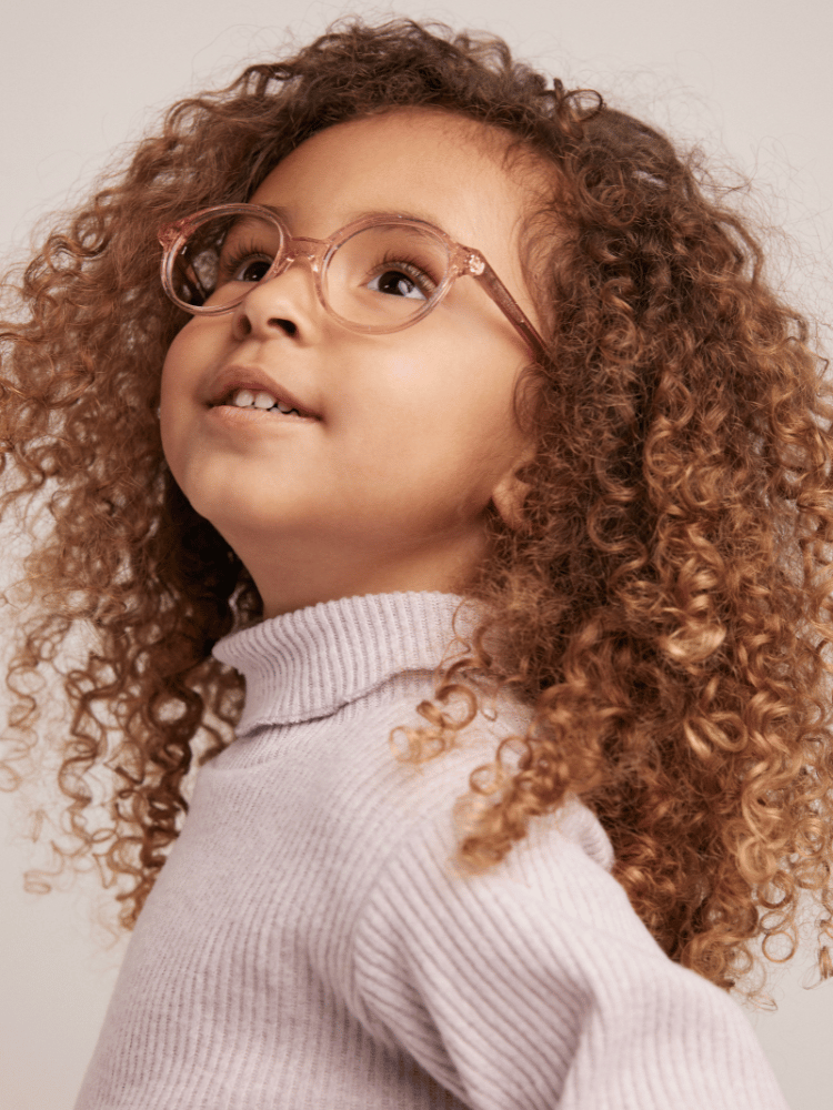 A little girl with curly hair wearing glasses and a turtleneck sweater.
