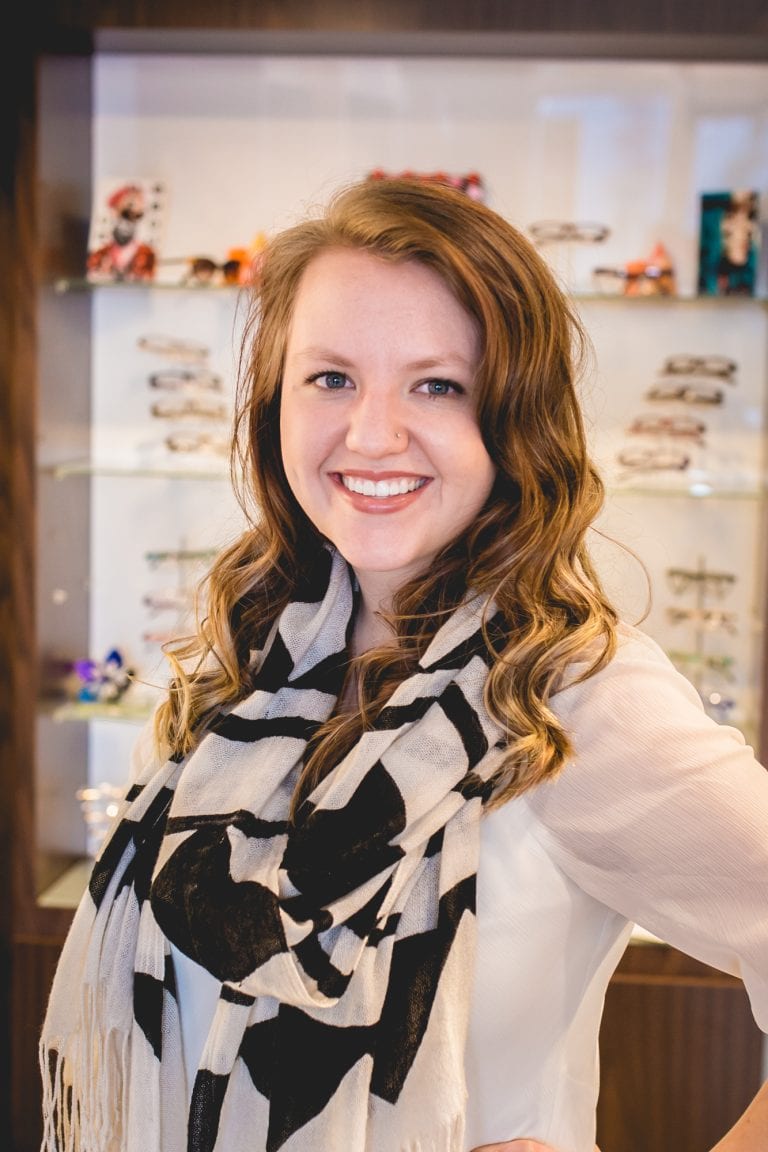 A woman wearing a scarf and a white shirt is standing in front of a display case.