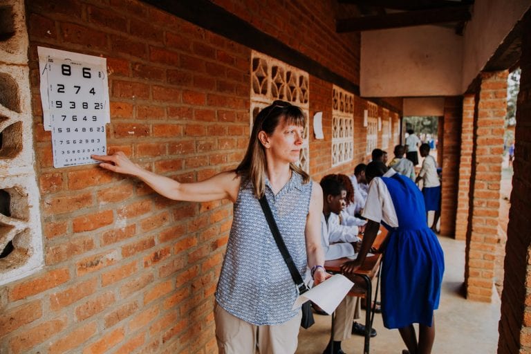 A woman is standing in front of a brick wall holding a piece of paper.