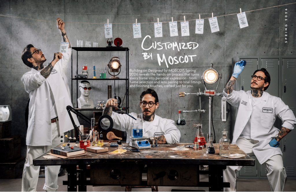 Three scientists in lab coats pose in a cluttered lab, testing colorful liquids under the words “Customized by Moscot.”