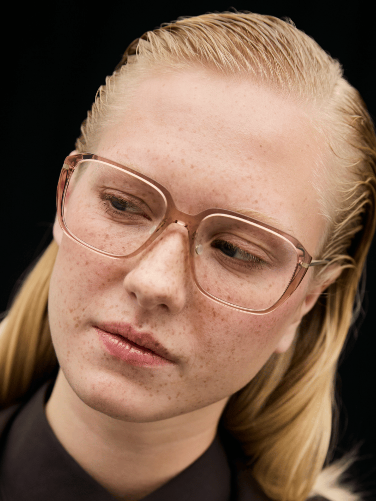 Close-up of a person with blond hair and glasses, looking down against a dark background.