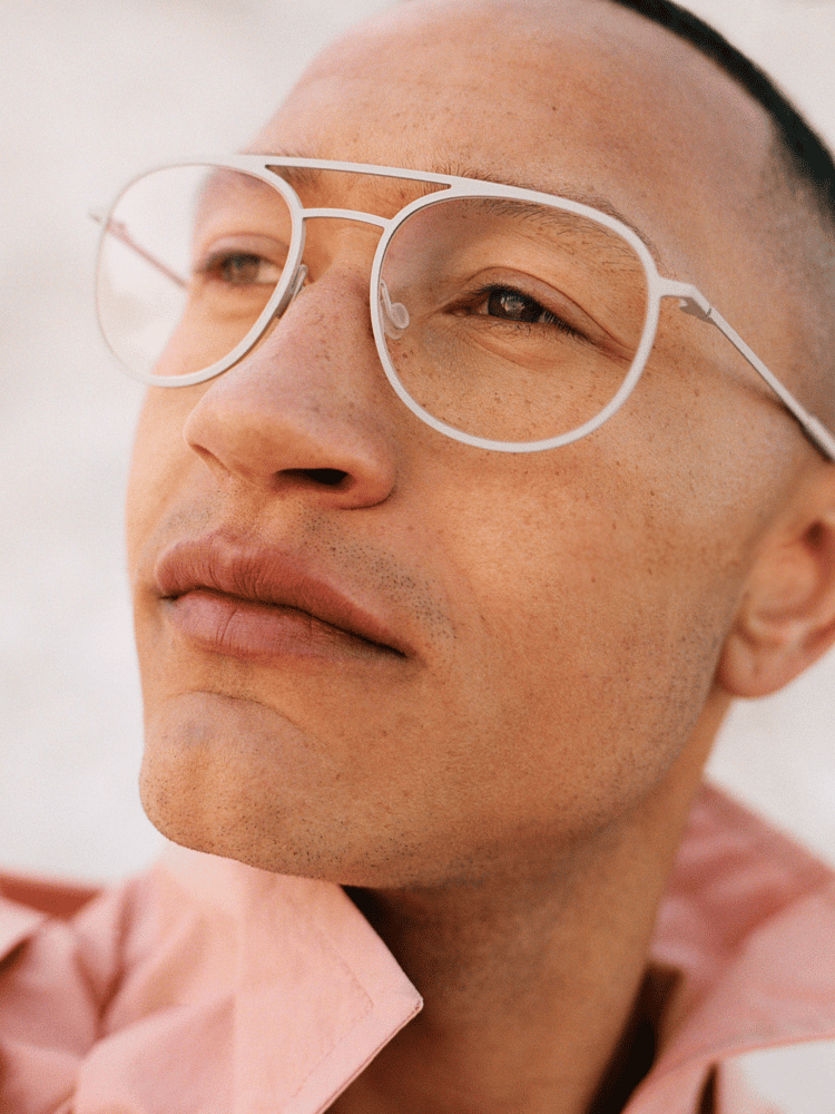 Close-up of a person wearing clear round glasses and a pink shirt, looking upward outdoors