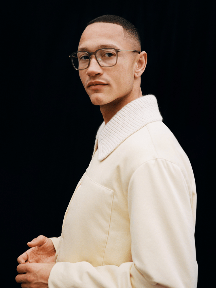 Portrait of a man in glasses and cream sweater against a black background