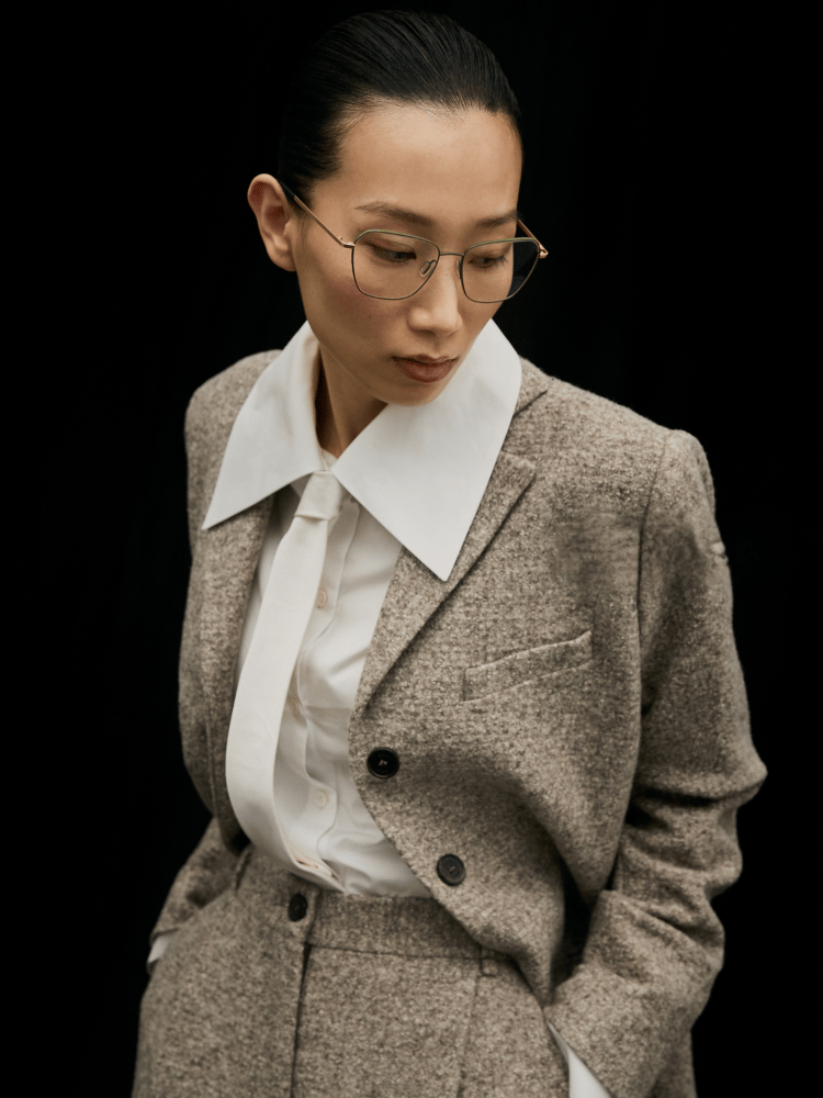Portrait of a person in a beige suit and white shirt, looking downward against a dark background
