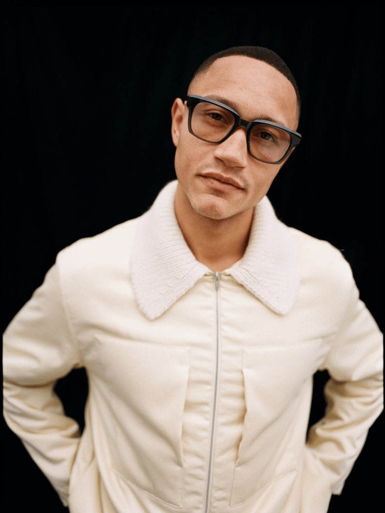 Man in white zip-up jacket and glasses posing against a black background