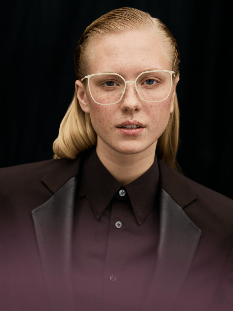 Person in a black suit and clear glasses against a dark background, with a calm expression.