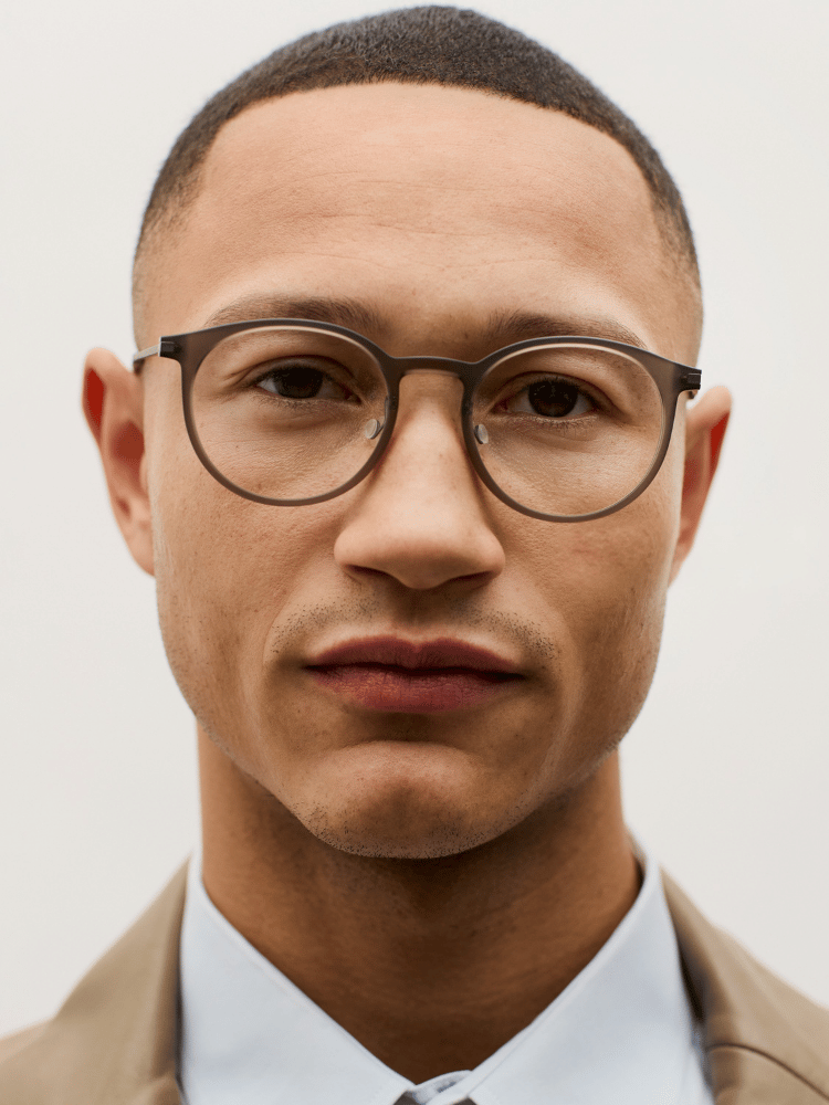 Portrait of a person wearing round glasses and a tan blazer against a light background
