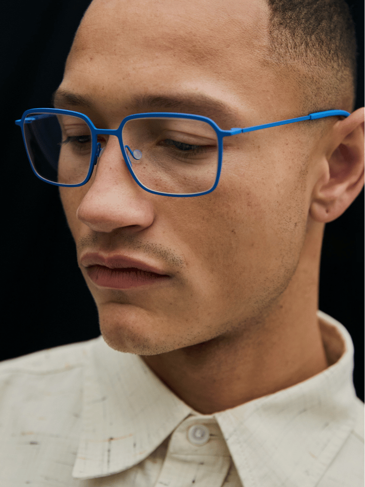 Person wearing bright blue glasses and a white shirt against a dark background
