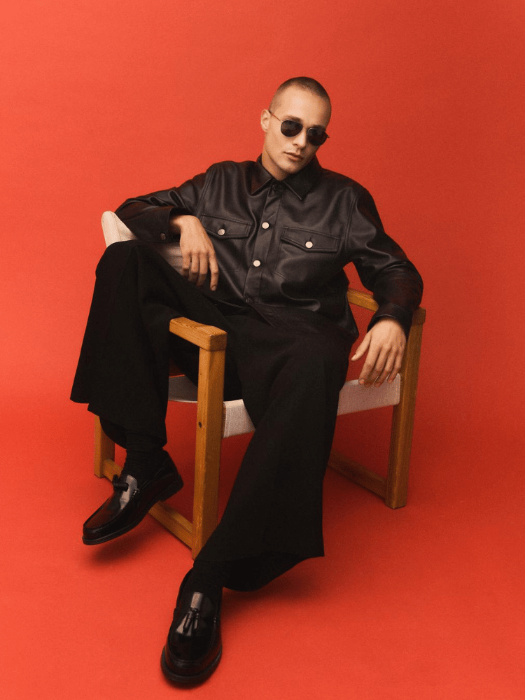 A man is sitting in a chair with his legs crossed and wearing sunglasses.