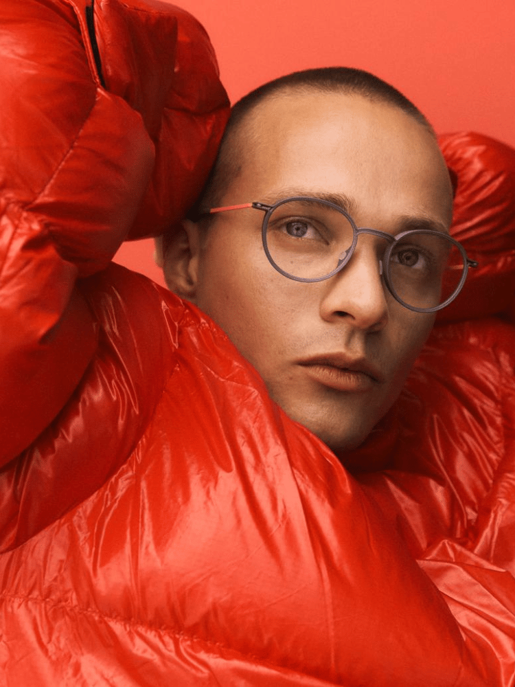 A man wearing glasses and a red jacket is wrapped in a red blanket.