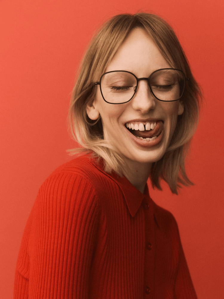 A woman wearing glasses and a red sweater is laughing.