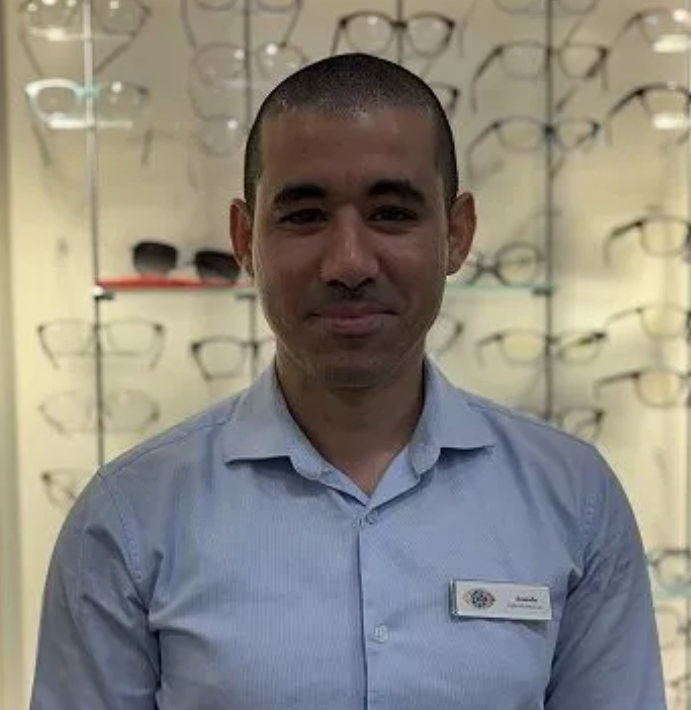 A man in a blue shirt is standing in front of a wall of glasses.