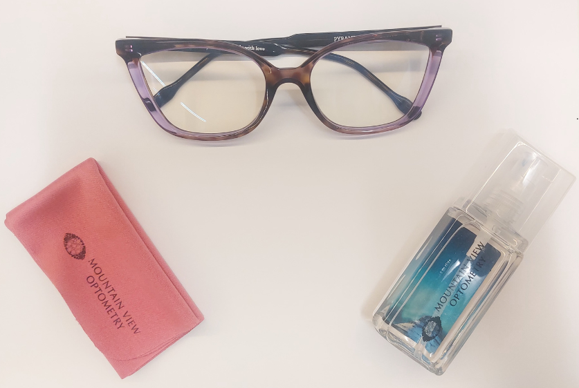 A pair of glasses next to a microfiber cloth and a spray bottle