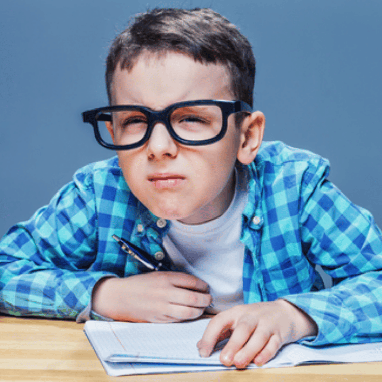 Boy in glasses writing at a desk, leaning forward with a focused expression.