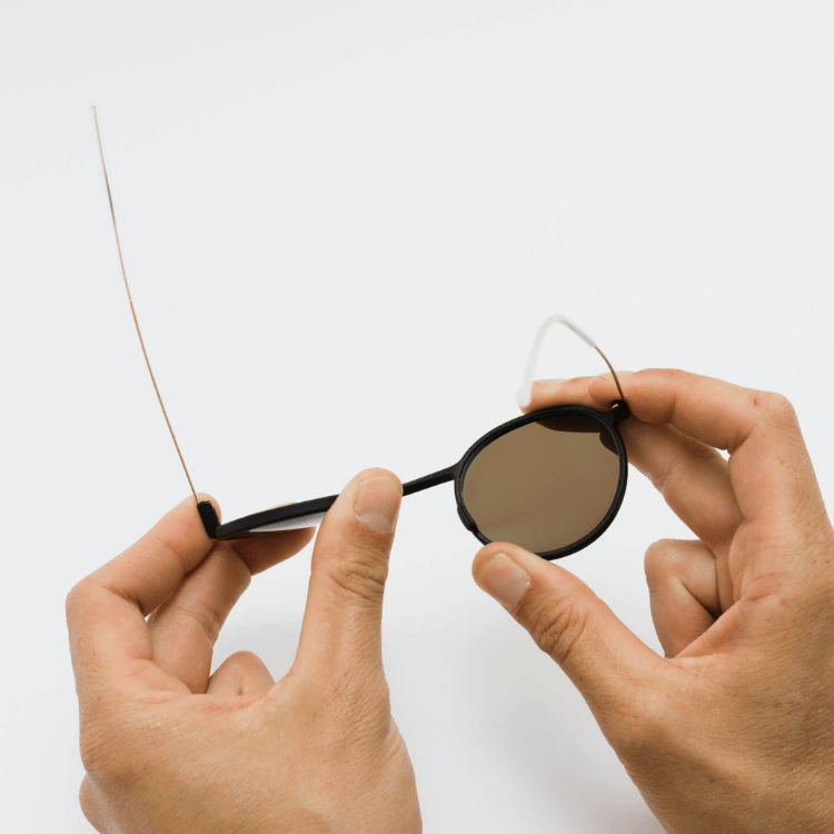 Hands adjusting the arms of round black sunglasses on a white background