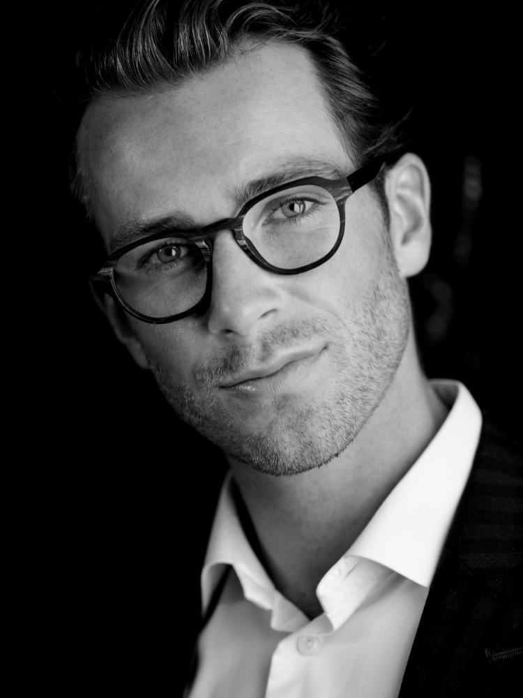 A black and white photo of a man wearing glasses and a white shirt