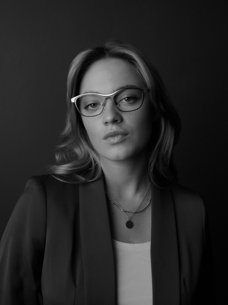 A black and white photo of a woman wearing glasses and a jacket.