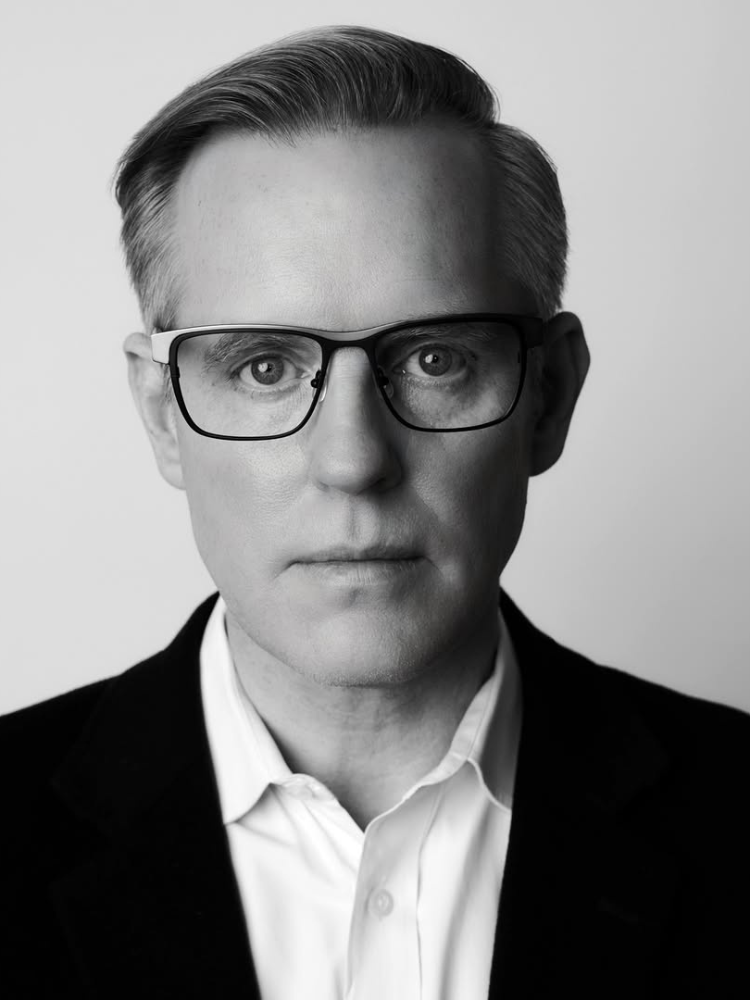 A black and white photo of a man wearing glasses and a suit