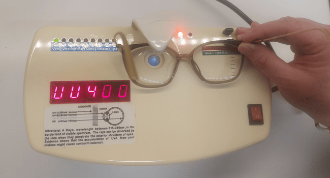 A person holding eyeglasses over an optical device displaying 