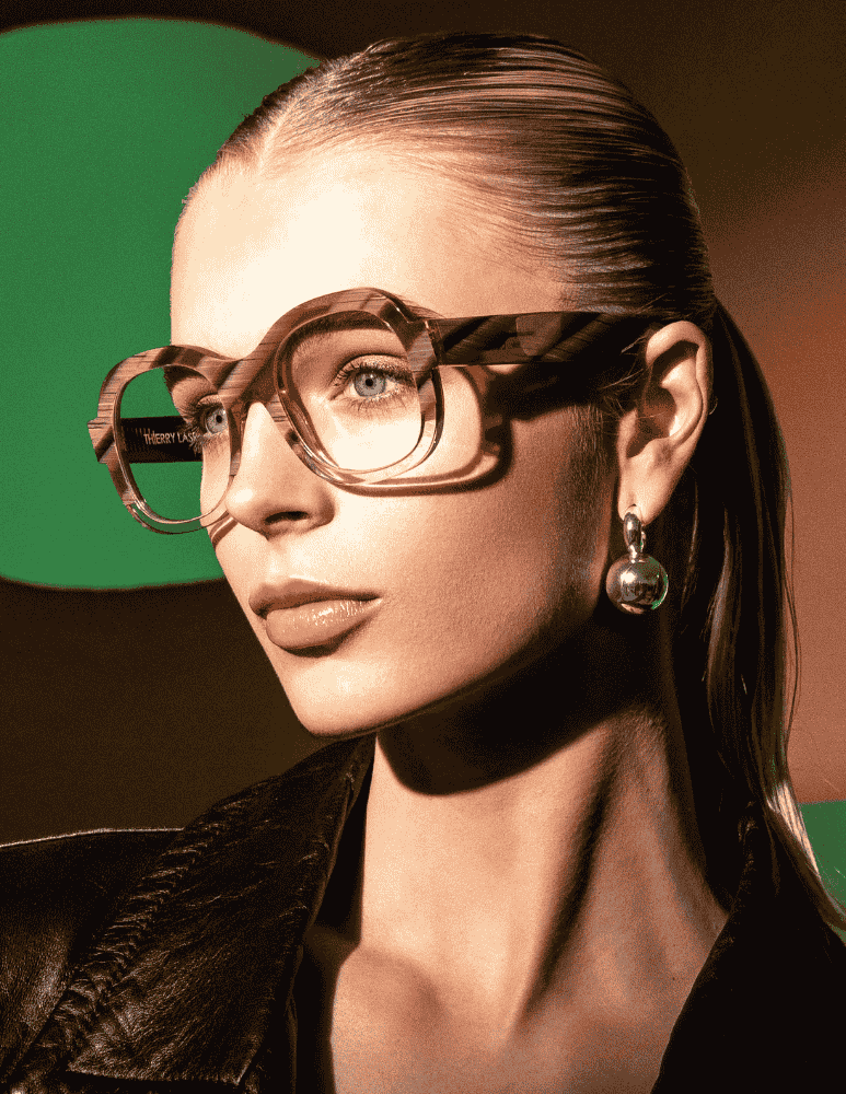 A woman wearing glasses and earrings is standing in front of a green background.