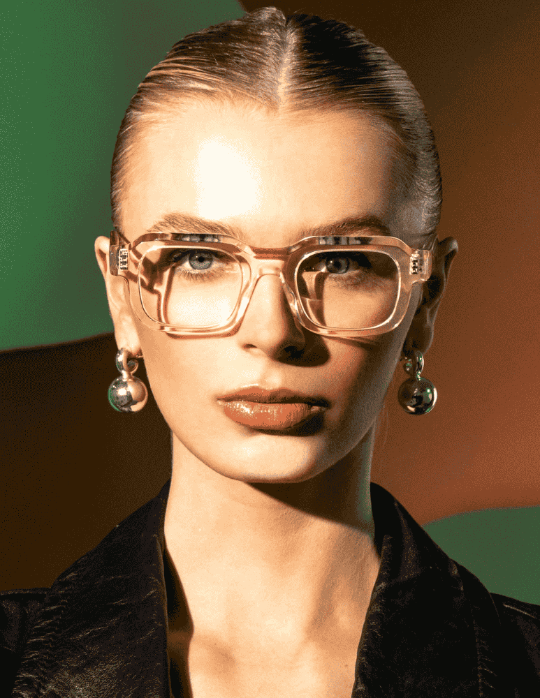 A woman wearing glasses and earrings is looking at the camera.