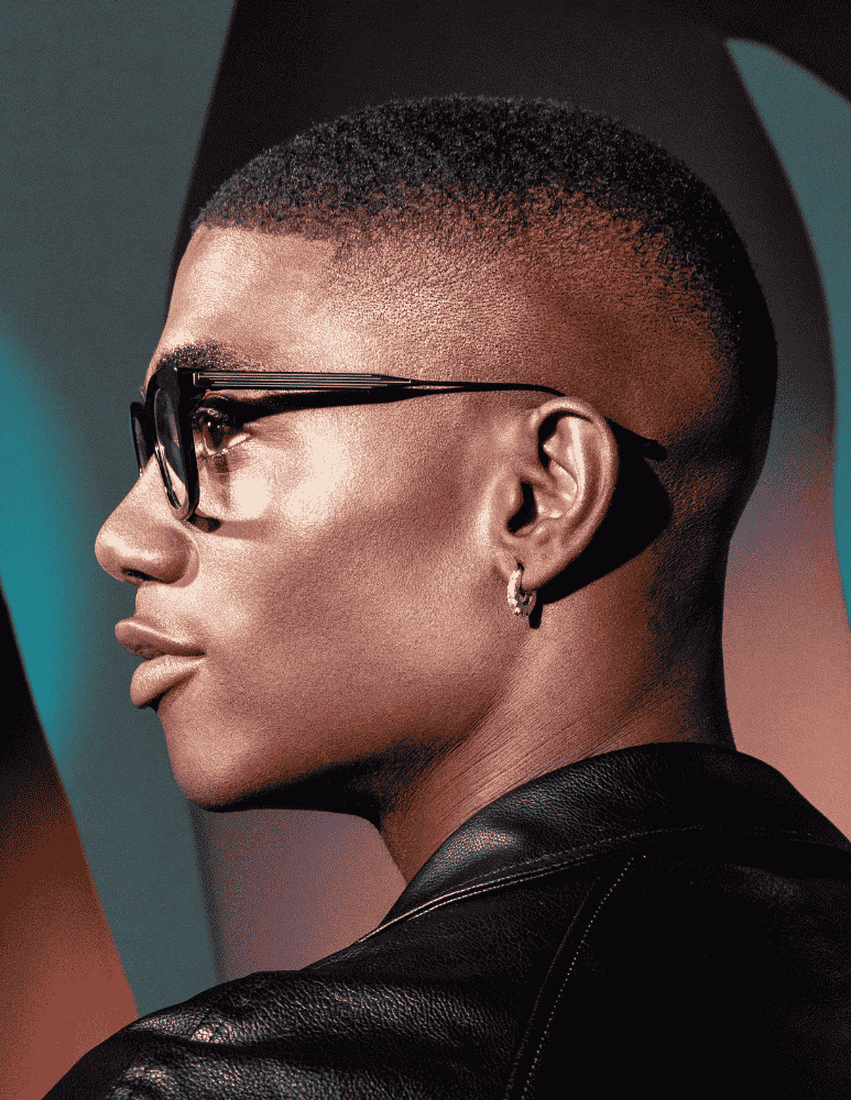 A man wearing glasses and a leather jacket is looking to the side.