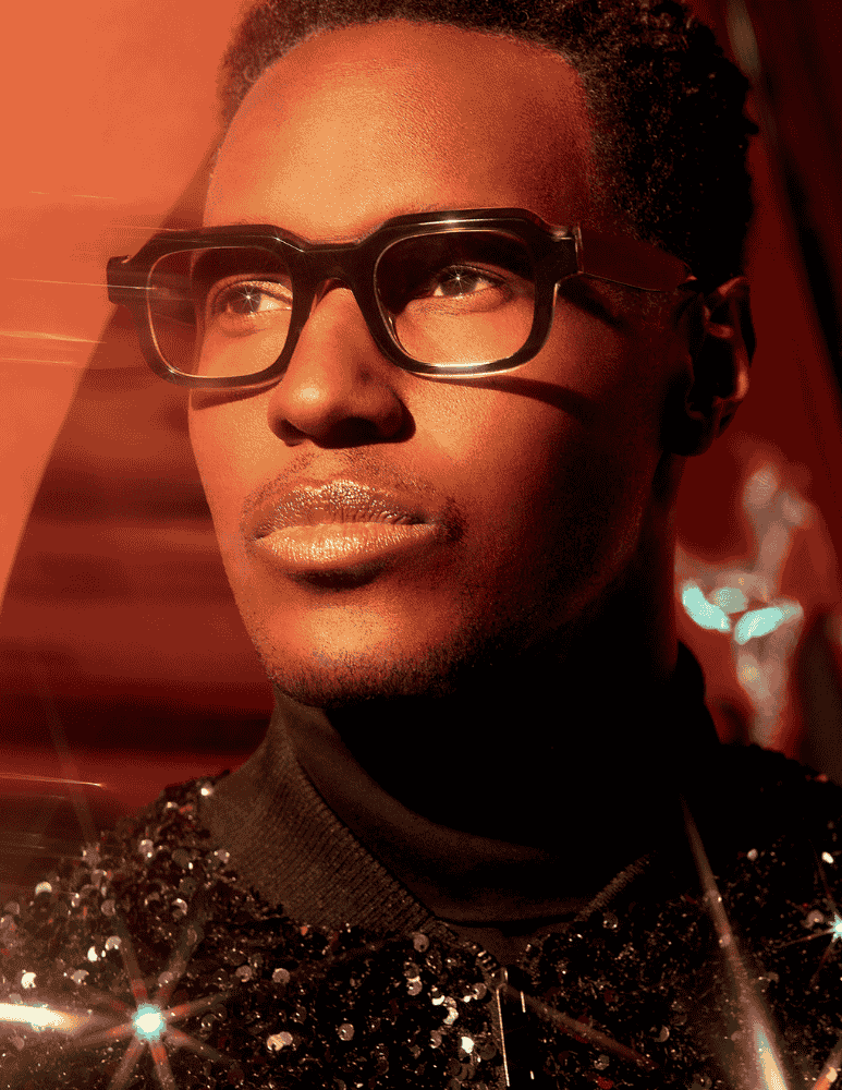 A close up of a man wearing glasses and a sequined jacket.
