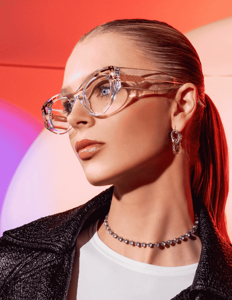 A woman wearing glasses and a necklace is standing in front of a red background.