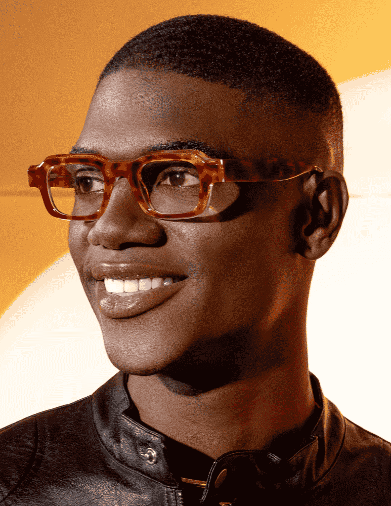 A man wearing glasses and a leather jacket is smiling