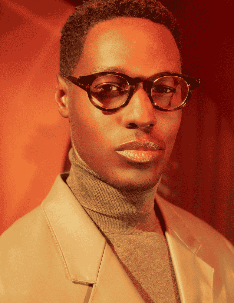 A man wearing glasses and a turtleneck is looking at the camera.
