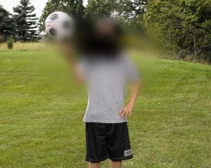 A young boy is juggling a soccer ball in a field.