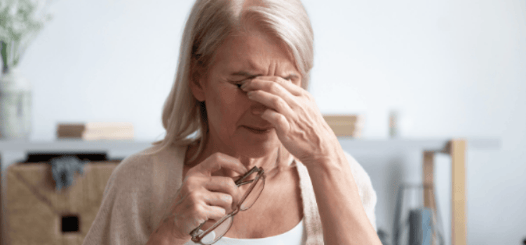 Woman holding eyeglasses, rubbing her eye, looking tired.