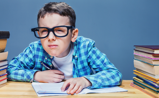 Child in oversized glasses reading at a desk, with stacked books on both sides.
