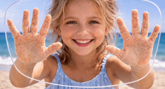 Smiling child with hands on a transparent surface, beach background.