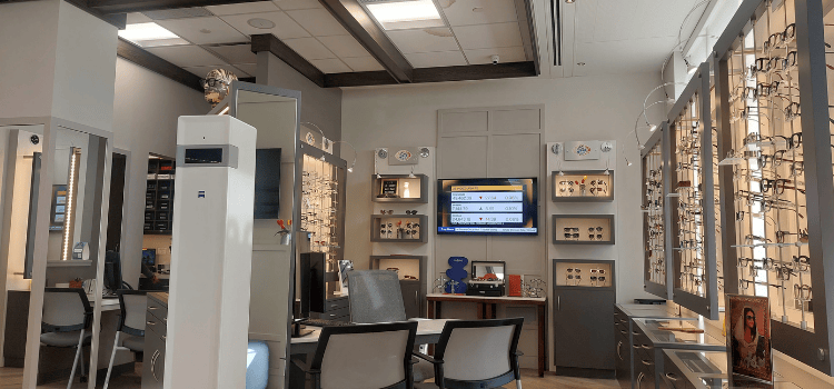 Modern optical store interior with glasses, frames, mirrors, and wall-mounted TV screens