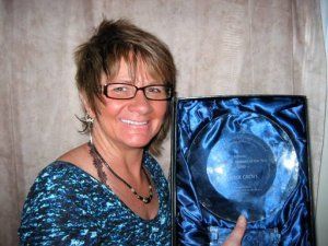 A woman wearing glasses is holding a blue plaque