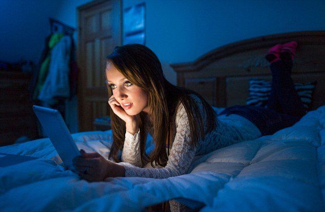 A woman is laying on a bed using a tablet computer.