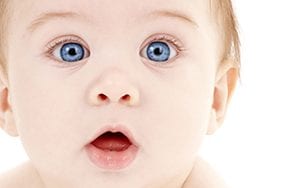A baby with blue eyes and a surprised look on his face.